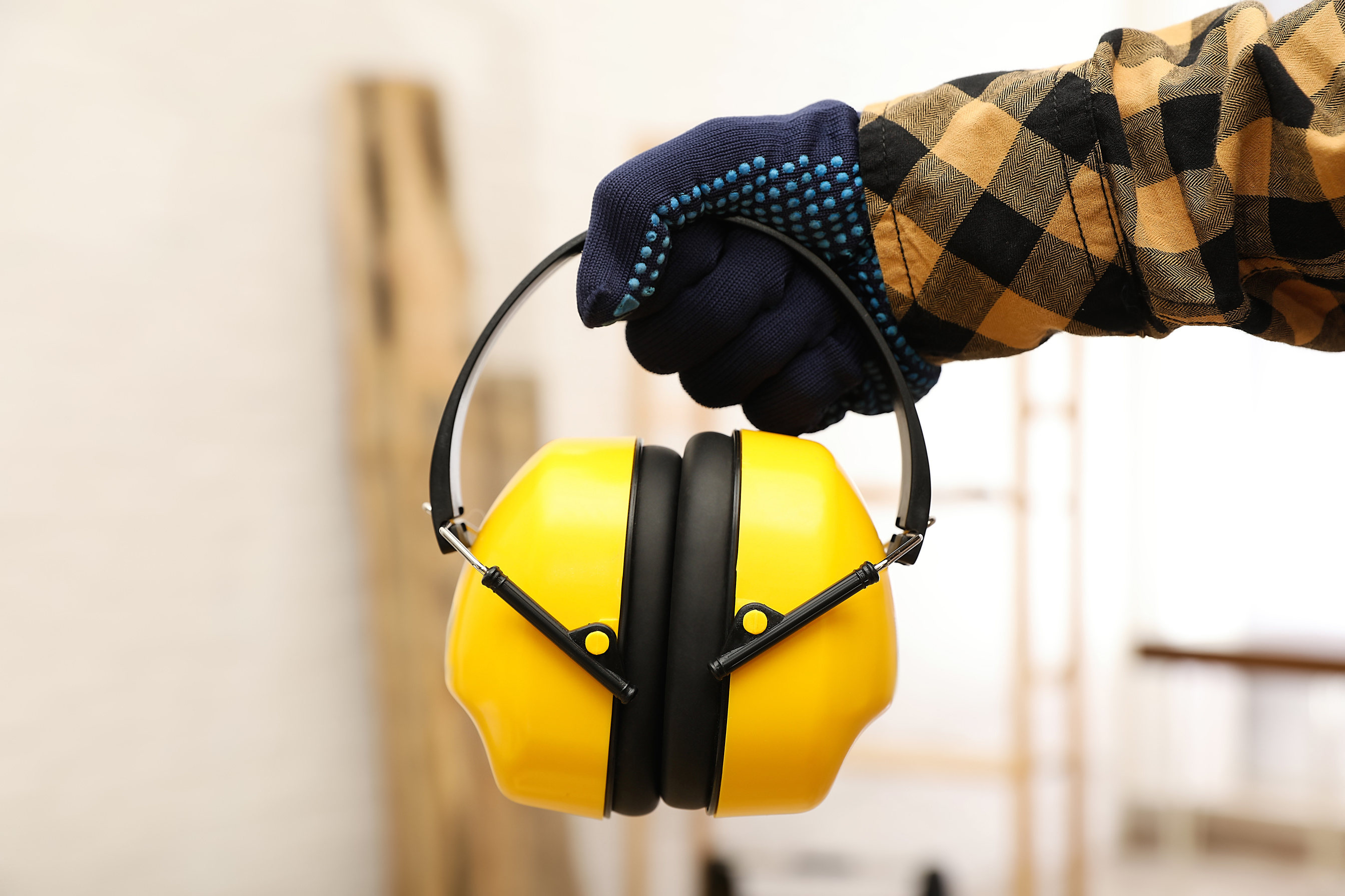 Worker Holding Safety Headphones Indoors, Closeup. Hearing Protection Device